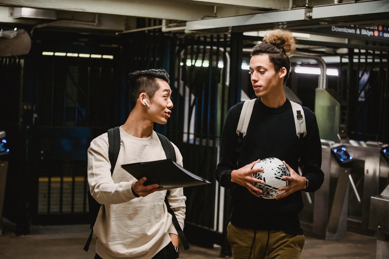 Two young men talk while holding a soccer ball in a subway station, embodying friendship and casual lifestyle.