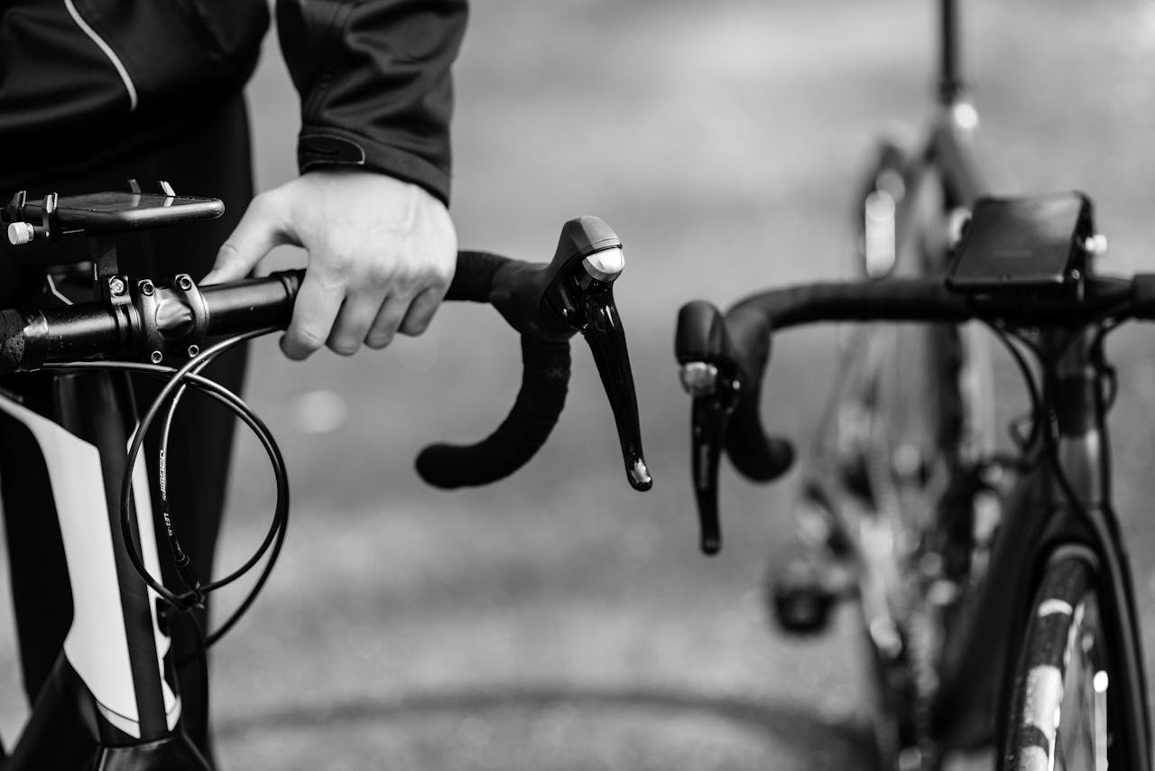 Black and white close-up of a cyclist gripping handlebars on a road bike outdoors.