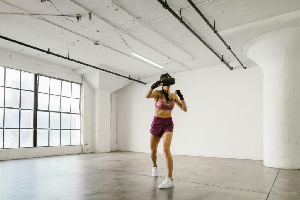 Adult woman using VR headset for fitness exercise in a modern indoor gym environment.